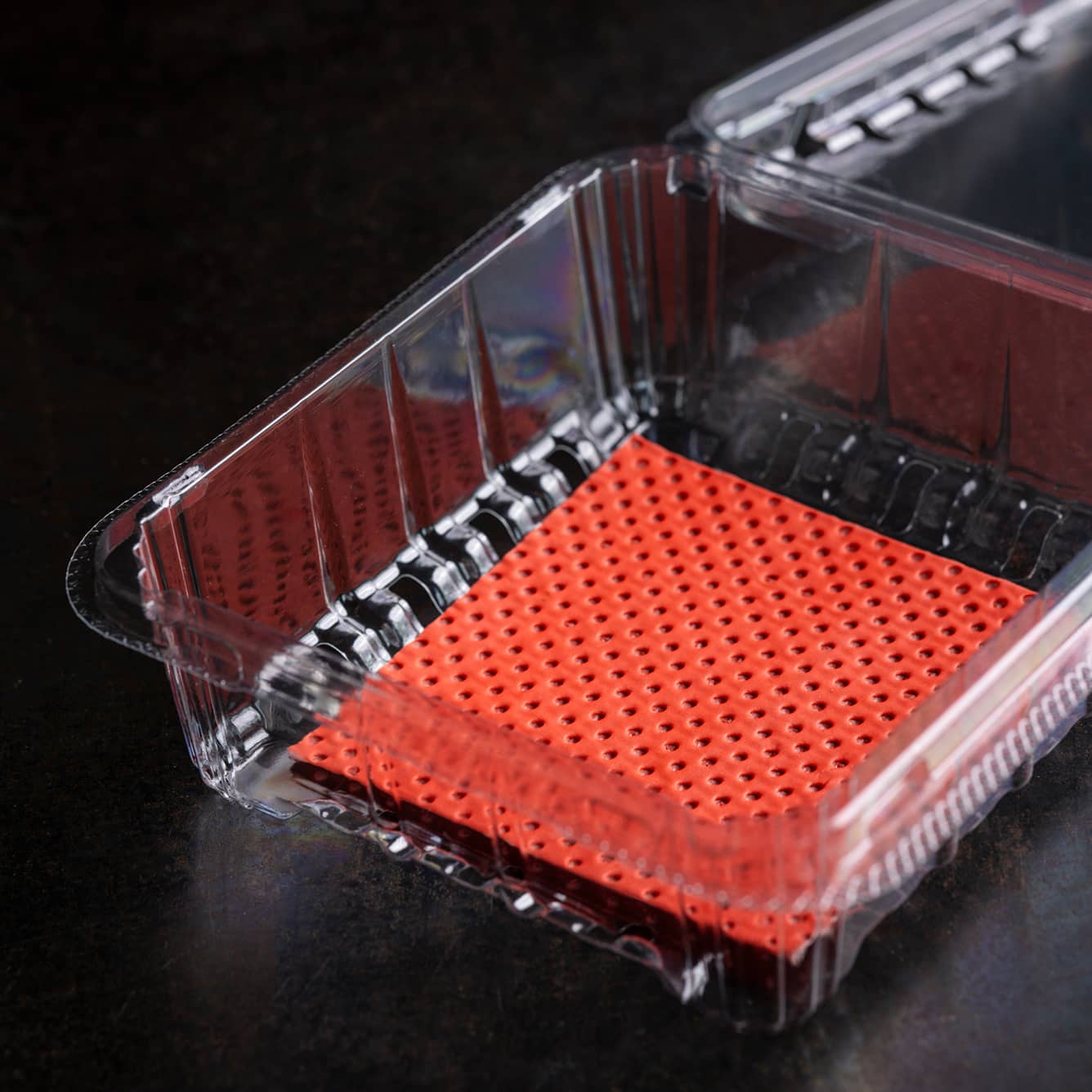 A Yucca Packaging clamshell punnet with a red absorbant pad insert inside.