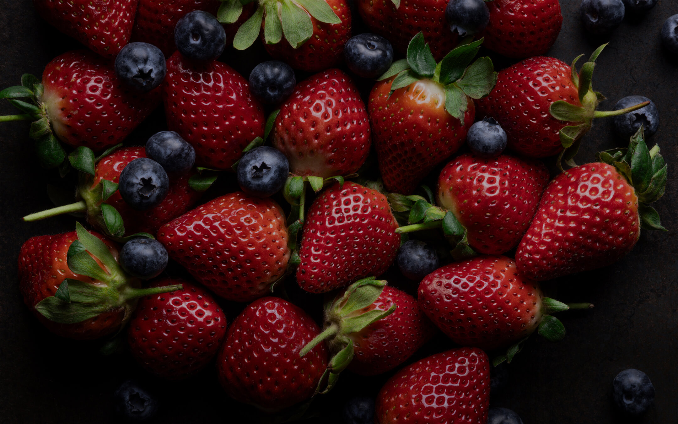 A dark moody artistic photograph of strawberries and blueberries.